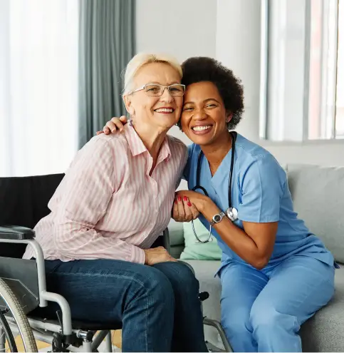 CNA and Elderly in a wheelchair holding hands and smiling together